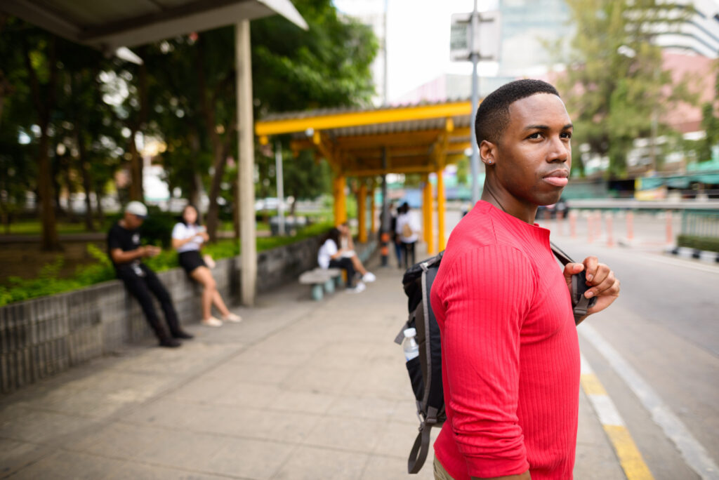 guy wearing red long sleeve shirt waiting at bus stop